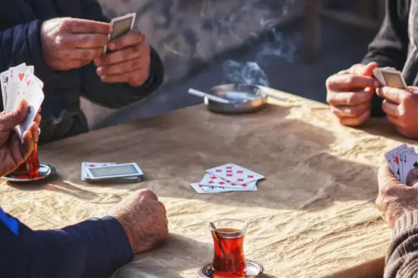 Four retired men playing a card game together around a table with glasses of tea
